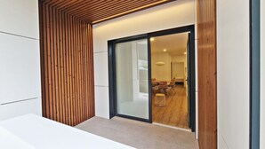 Un intérieur moderne avec un mur à lattes de bois, une porte en verre donnant sur un coin repas comprenant une table et des chaises, et un banc blanc.