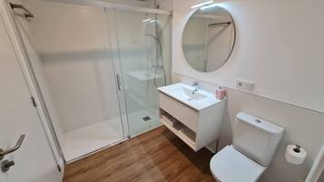 Un bagno moderno con cabina doccia in vetro, un lavandino bianco e un water.