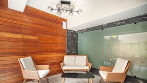 Habitació moderna amb paret de fusta, un separador de vidre i una taula de cafè negra. Hi ha dues cadires de vimetla amb coixins blancs.