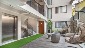 Un edifici modern amb terrassa de fusta, cadires de vimet i una escala.