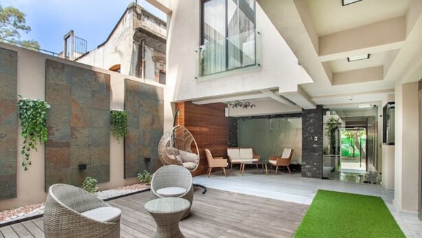 Zona exterior moderna amb mobles de vimet, gespa artificial verda i una paret de pedra amb plantes.
