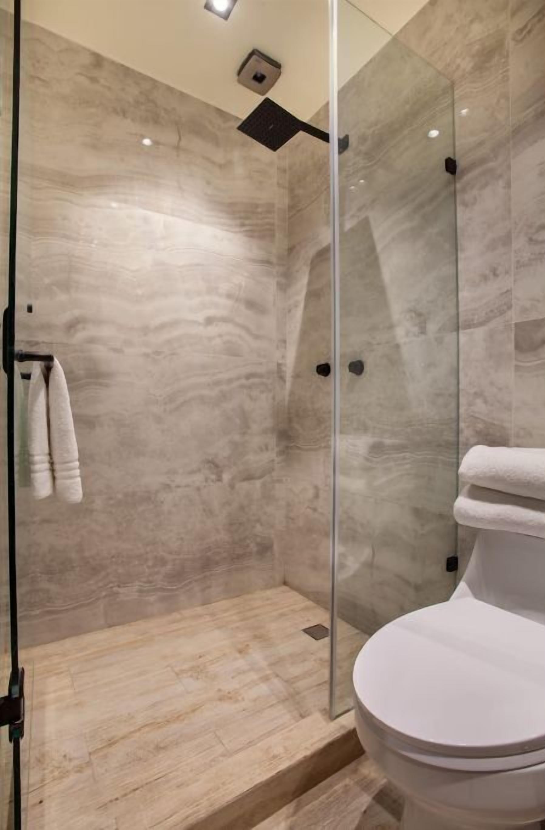 Une salle de bain moderne avec une douche à parois de verre, des murs en marbre et des toilettes blanches.