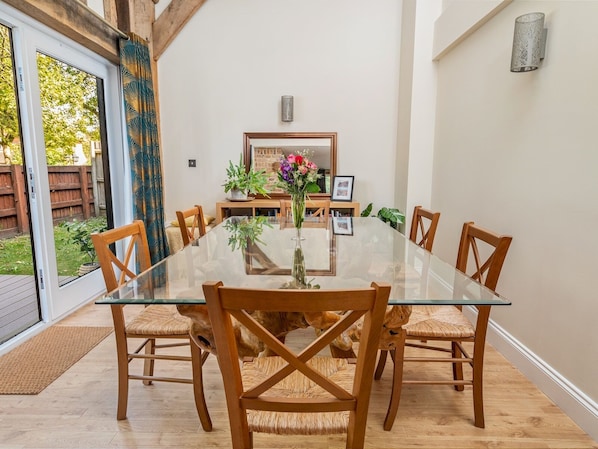 Un coin repas avec une table en verre entourée de chaises en bois, un vase rempli de fleurs et, au fond, une cheminée en briques.