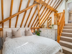 Une chambre avec un grand lit, des poutres en bois, une commode et un escalier.