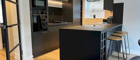 A modern kitchen with a central island, bar stools, and a window with blinds.
