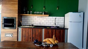 A kitchen with a wooden table, a green wall, a white tiled backsplash, and a white refrigerator. - Rua Professor Nelson Rabello (Marica)