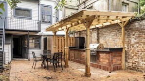 A backyard patio with a wooden pergola, a grill, and a dining area with chairs and a table. - Pet-Friendly 1855 Garden Retreat • Savannah (Savannah)