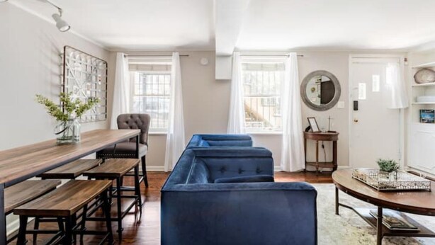 A modern living room with a wooden dining table, blue sofa, and a large mirror. - Pet-Friendly 1855 Garden Retreat • Savannah (Savannah)