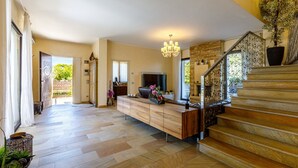 A spacious living area with a wooden staircase, a TV, and a dining area with a bench.