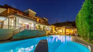 A modern villa with a swimming pool, outdoor seating, and a well-lit patio area.