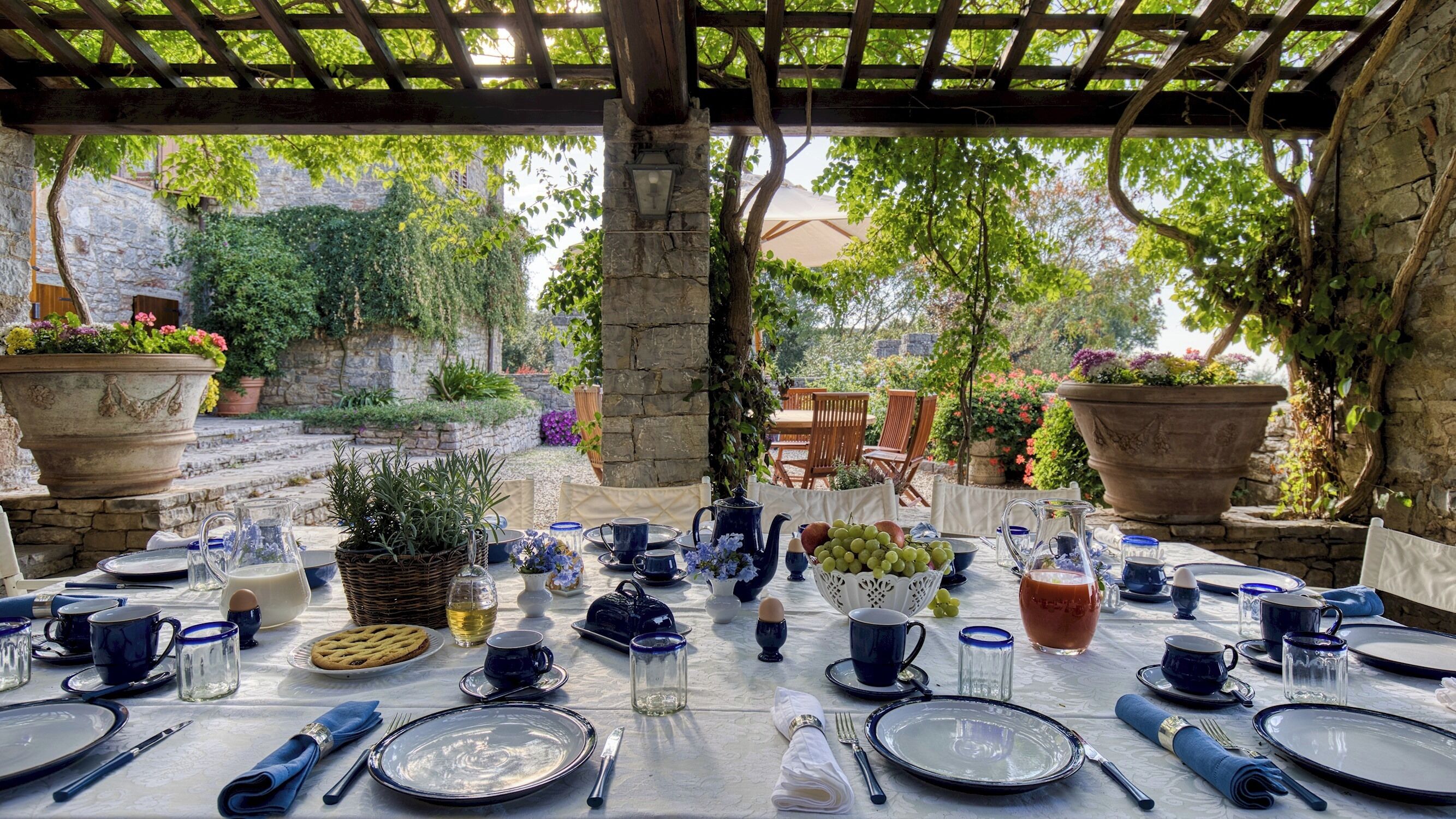 An outdoor dining area with a pergola, stone walls, and potted plants.