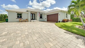 Una casa de dos pisos con entrada pavimentada, un garaje y un pequeño patio con sillas.