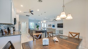 Una cocina moderna con armarios blancos, encimera de granito y comedor con mesa y sillas de madera.