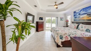 Un dormitorio con una cama, ventilador de techo, un ventanal grande y un cuadro en la pared.