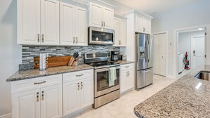 Cocina moderna con armarios blancos, electrodomésticos de acero inoxidable, encimeras de granito y una salpicadera azulejada.