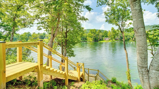 Eine Holzterrasse, die zu einem See mit Bäumen und einem entfernten Haus führt.
