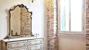 A bedroom with a white dresser, a large mirror, and a brick wall. - Casa particular vintage (Rome)