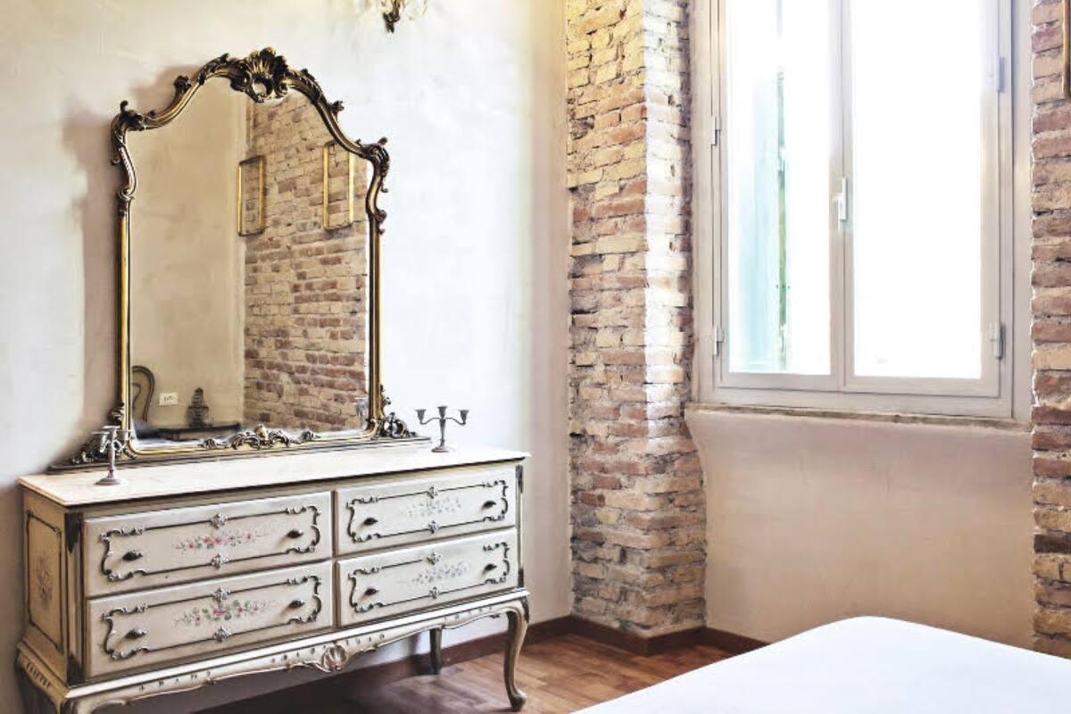 A bedroom with a white dresser, a large mirror, and a brick wall.