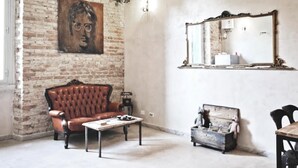 A room with a brick wall, a leather sofa, a small table, a vintage suitcase, and a mirror. - Casa particular vintage (Rome)