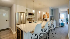 A modern kitchen with white cabinetry, stainless steel appliances, and a central island with bar stools. - Oceanfront Watsonville Condo w/ Beach Access! (Watsonville)