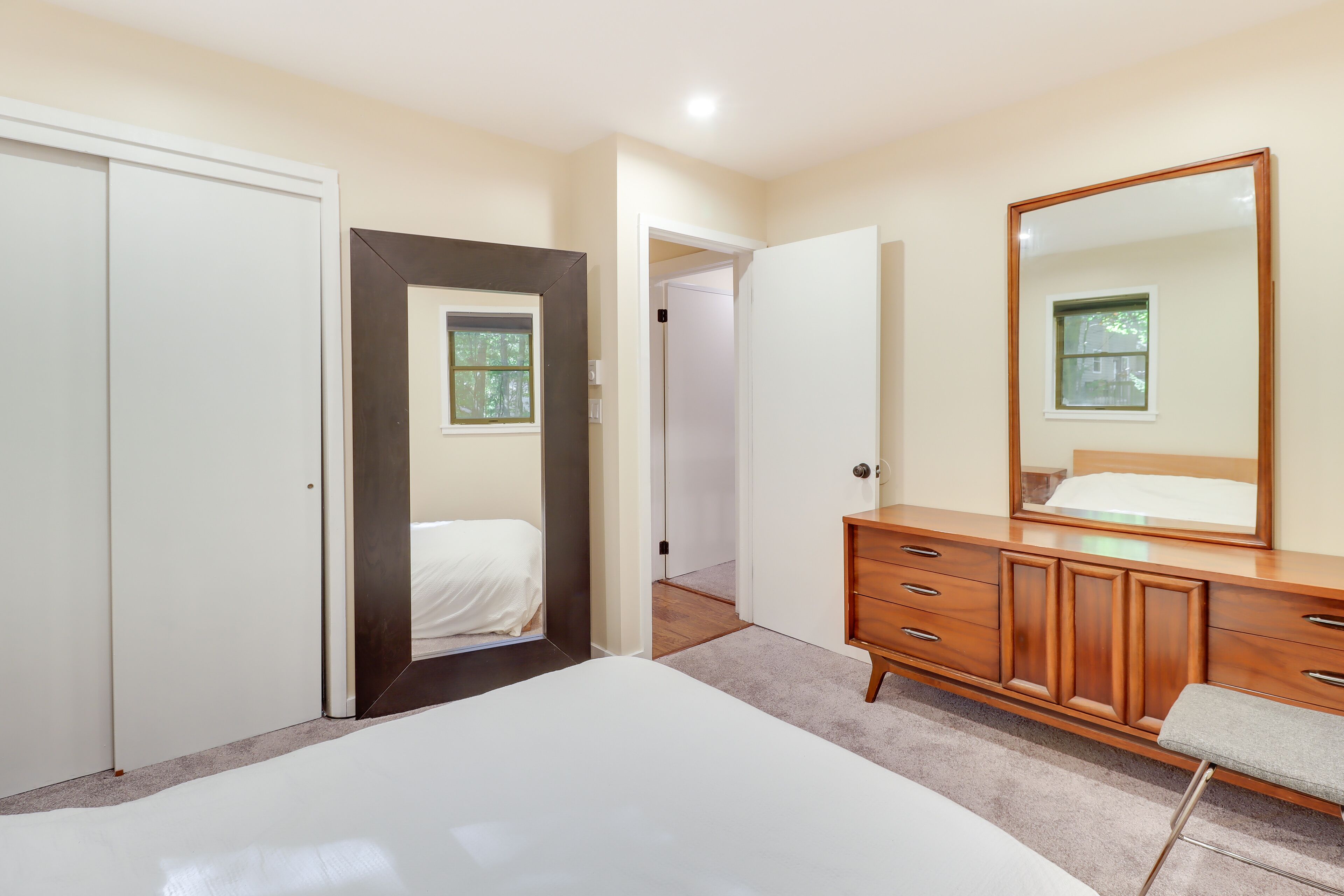 A bedroom with a bed, a dresser, a mirror, and a door leading to another room.
