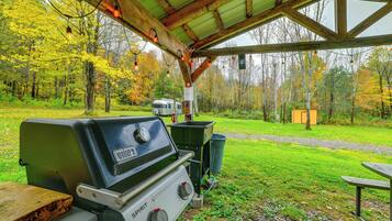An outdoor grill area with a covered pavilion, a trash bin, and a picnic table.