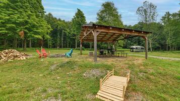A covered outdoor area with picnic tables, a grill, and a camping trailer.