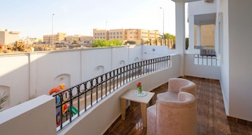 Un balcón con vistas a edificios, una mesa con un florero y dos sillas.