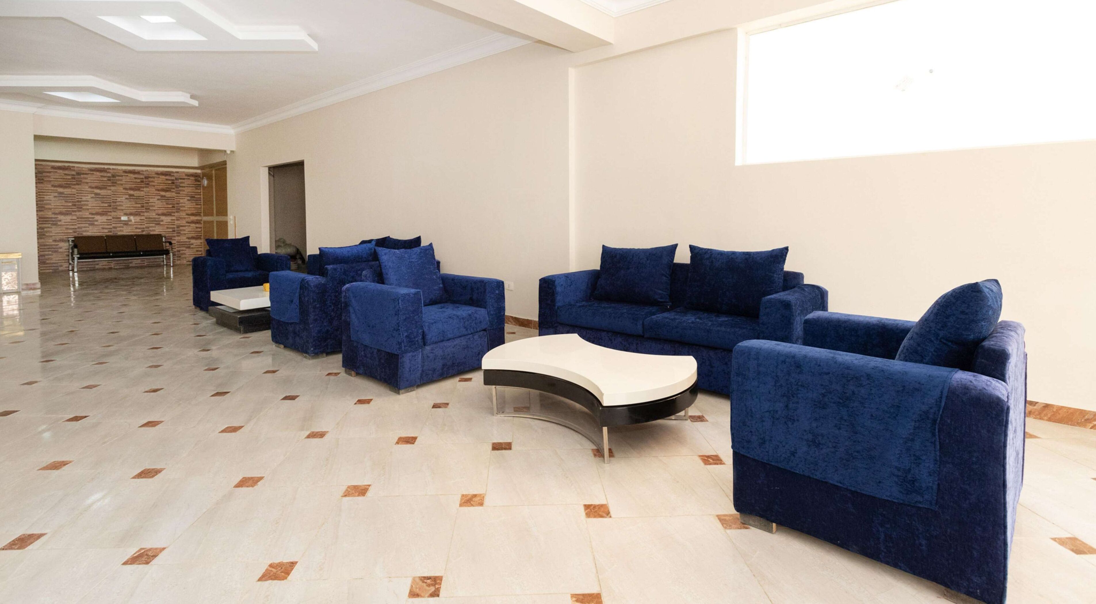 A spacious room with a modern design, featuring a seating area with blue sofas and armchairs, a white coffee table, and a patterned wall.