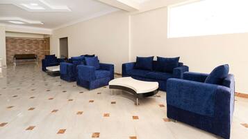 A spacious room with a modern design, featuring a seating area with blue sofas and armchairs, a white coffee table, and a patterned wall.