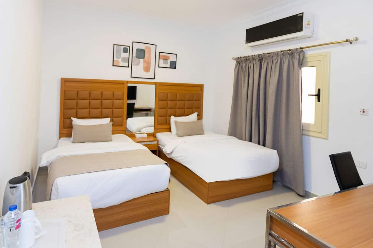 A hotel room with two beds, a desk, a chair, a coffee maker, and a water dispenser.