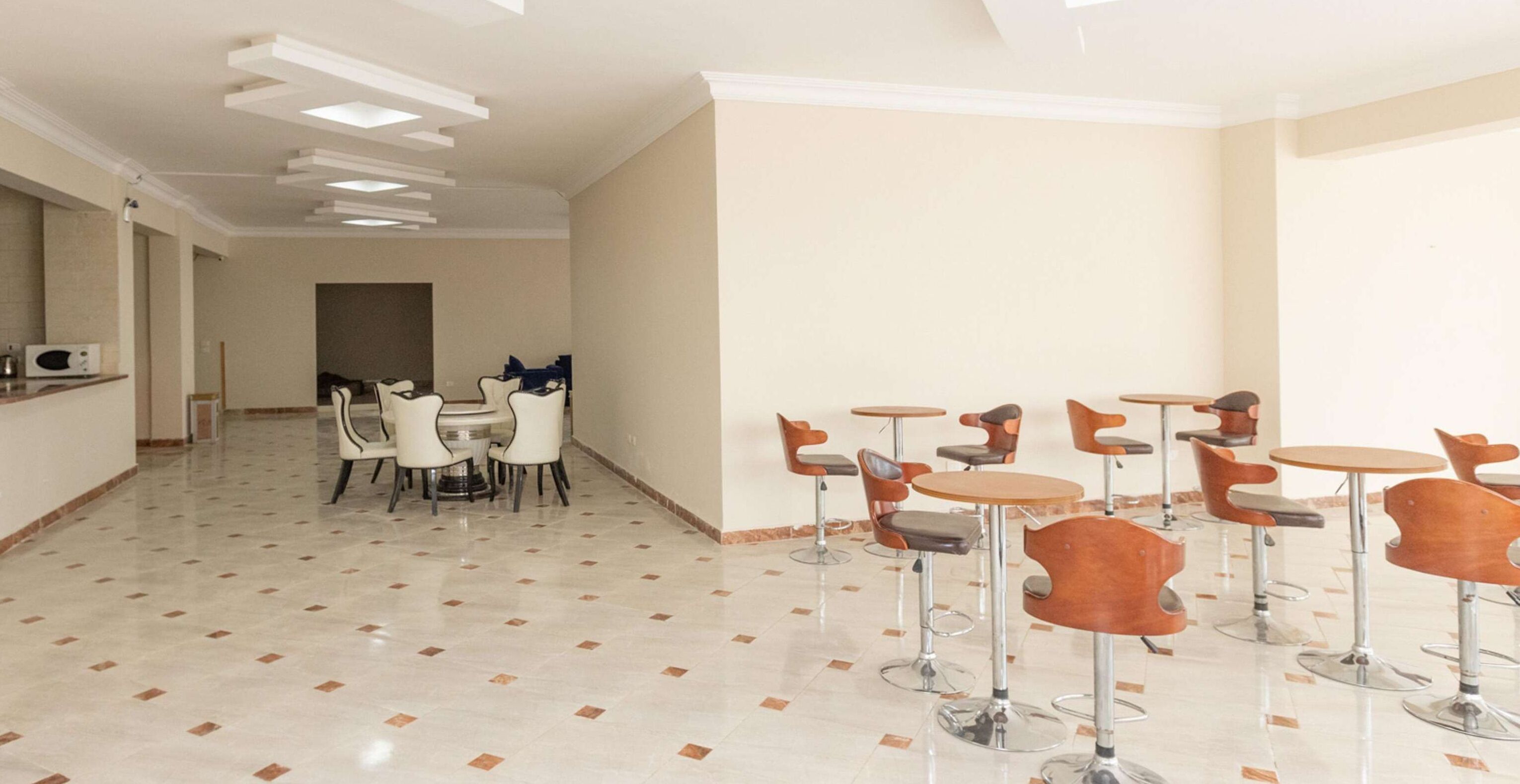 Una habitación amplia con suelo de baldosas, una zona de comedor con una mesa redonda y sillas, y una barra con taburetes.