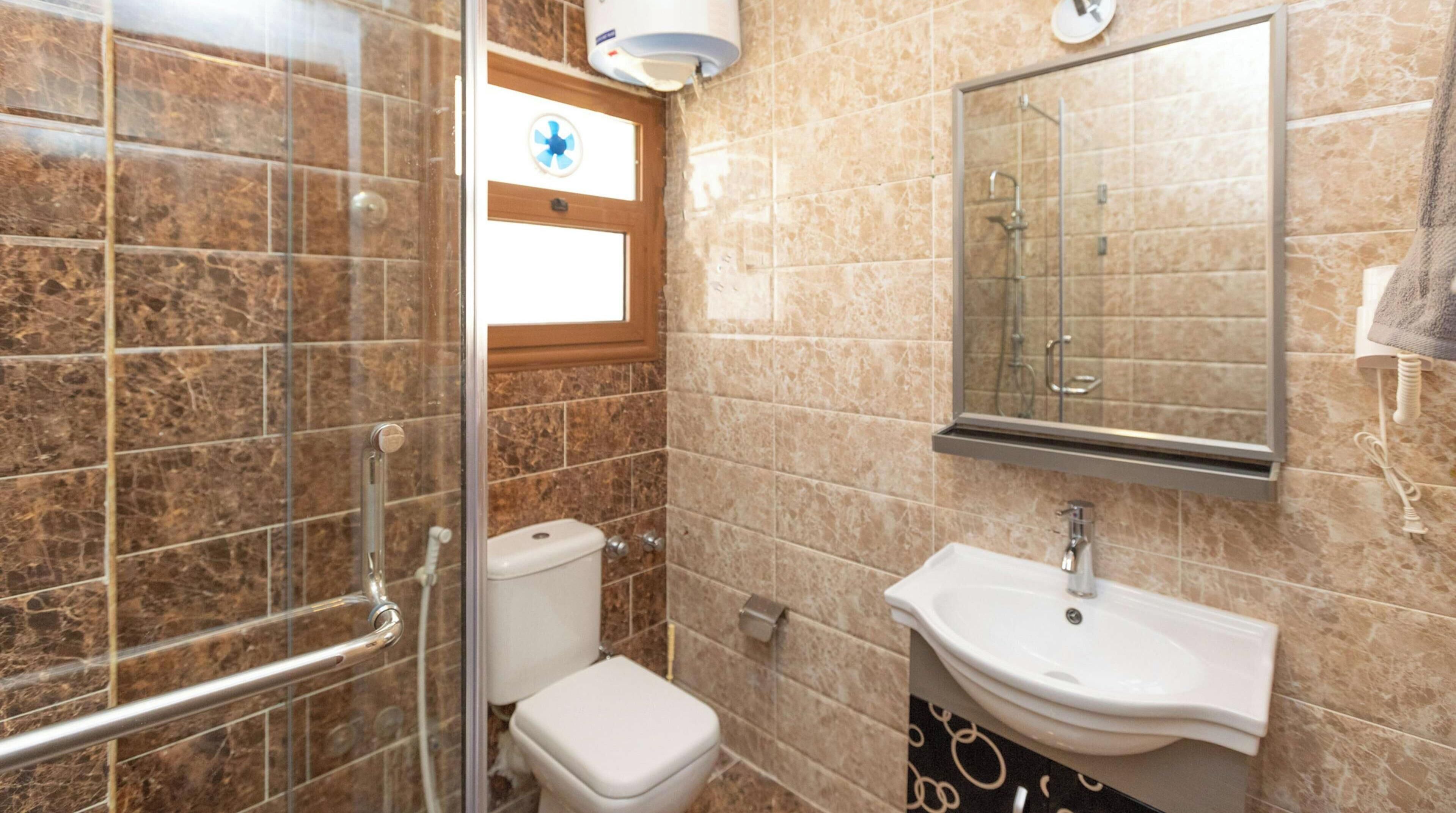 A bathroom with a glass shower enclosure, a toilet, a sink, and a mirror.