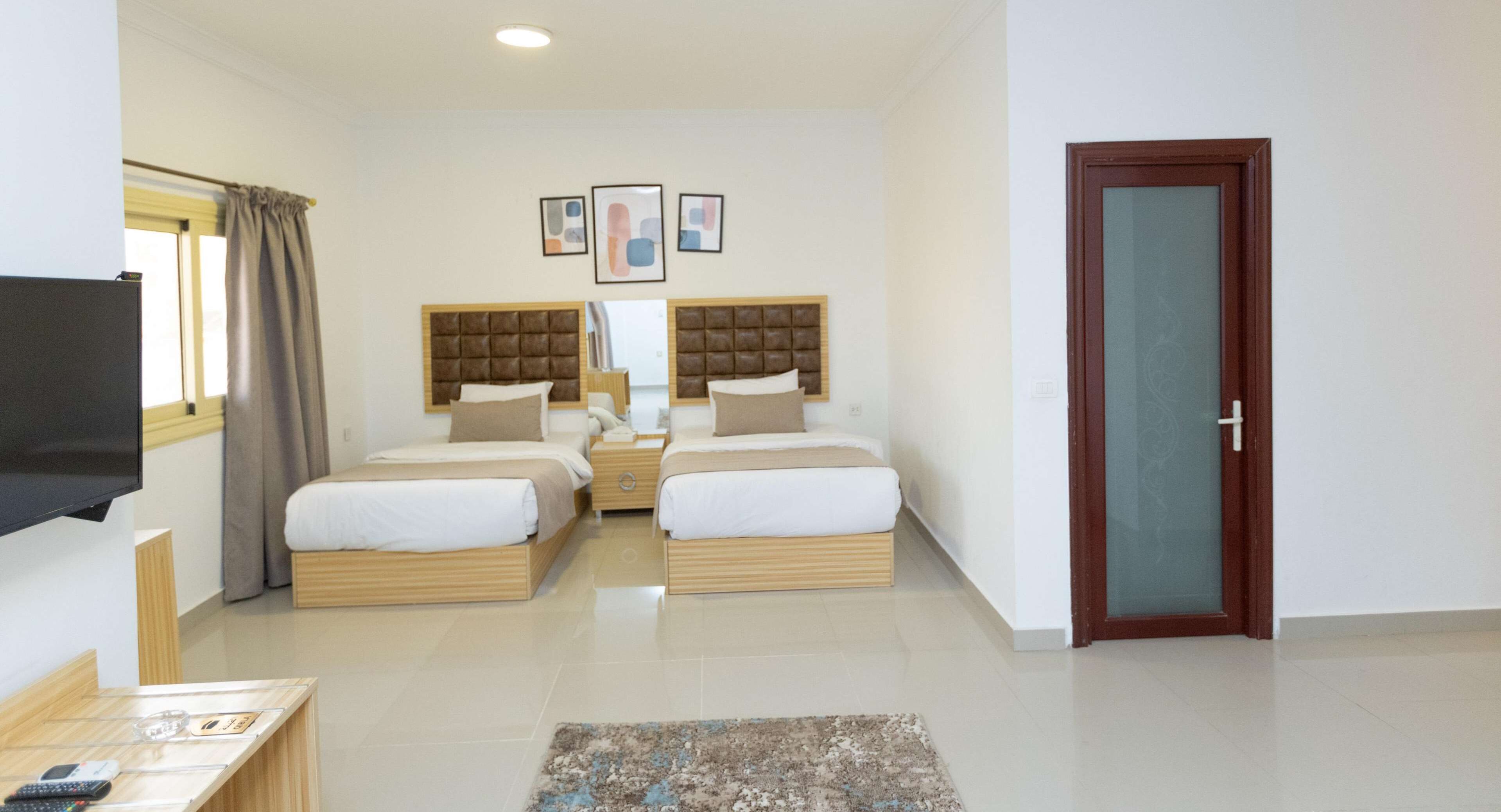 A hotel room with two beds, a TV, a desk, and a door.