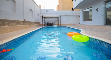 Una piscina con agua azul cristalina, rodeada de muros blancos y una base de piedra.