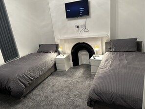 Ein modernes Schlafzimmer mit zwei Einzelbetten, einem flachbildfernseher über dem Kamin und Nachttischlampen.