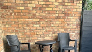 Ein Patio mit einer Ziegelmauer, einem kleinen runden Tisch und vier Korbstühlen und Hocker.