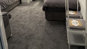 Ein Hotelzimmer mit zwei Betten, einem an der Wand montierten Fernseher, einem Kamin und einem Metallregal mit Gegenständen darauf.
