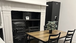 Ein Essbereich mit einem Holztisch, vier Stühlen, einer Topfpflanze, einem schwarzen Schrank und einem weißen Kamin mit dekorativen Verzierungen.