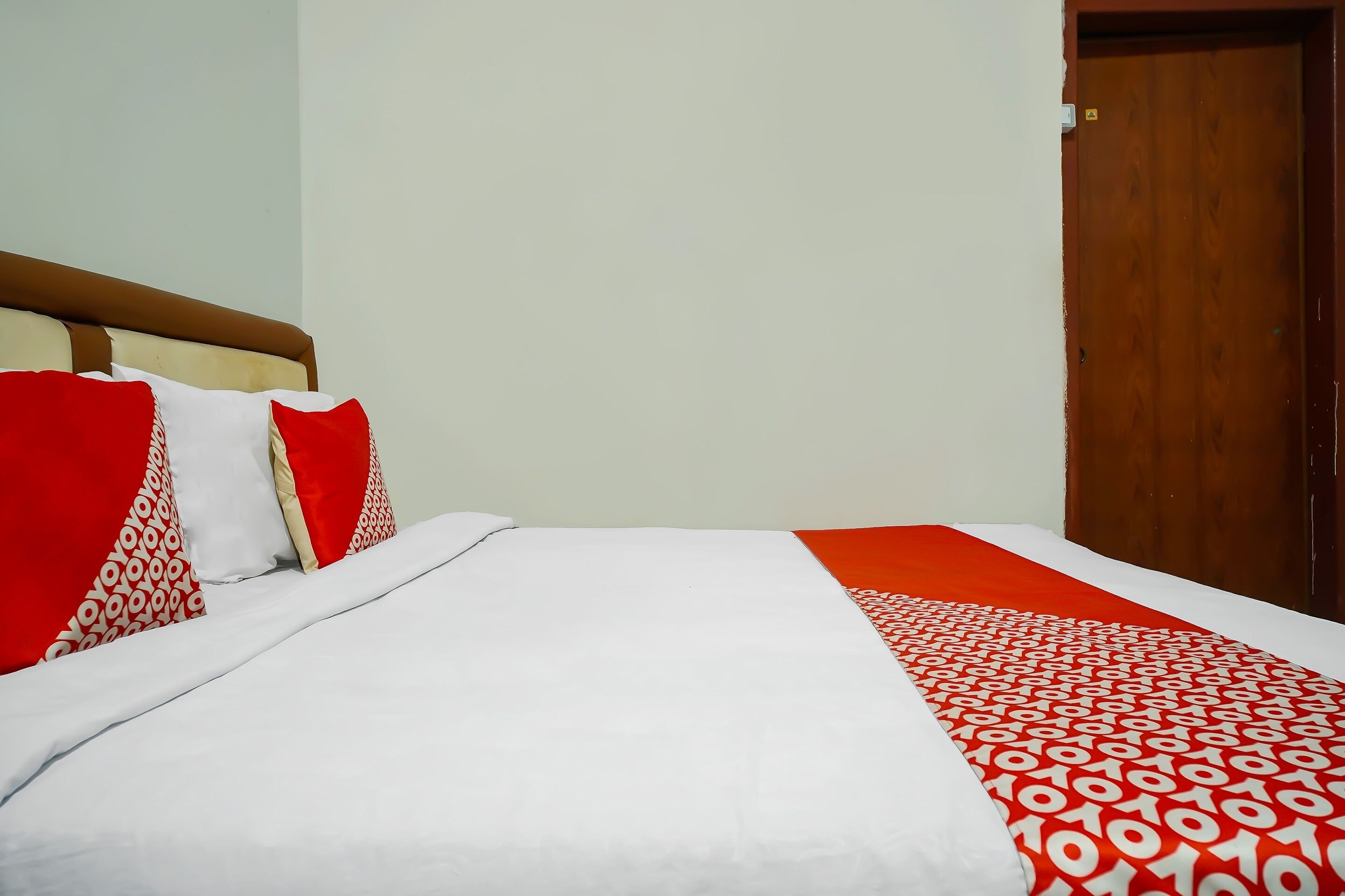 A bed with white and red bedding, a wooden headboard, and a red door in the background.
