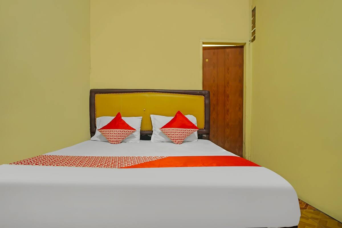 A bed with a white and orange bedspread, two red pillows, and a wooden headboard.