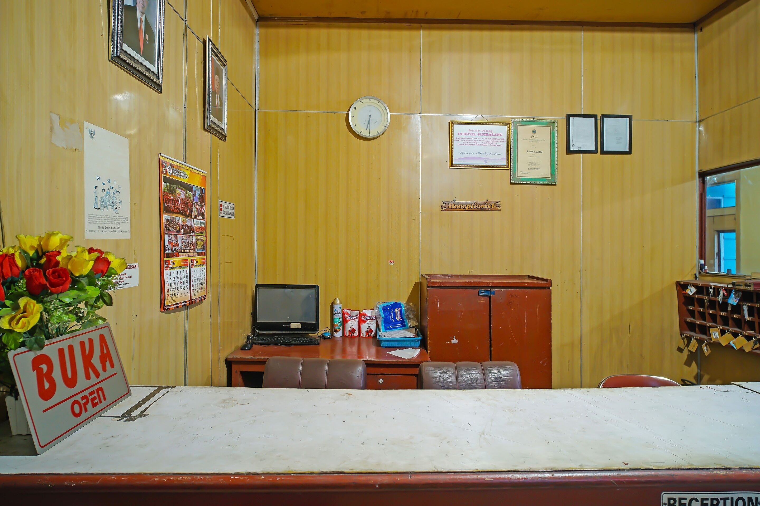 A reception area with a desk, a clock, framed certificates, and a sign indicating the room is open.