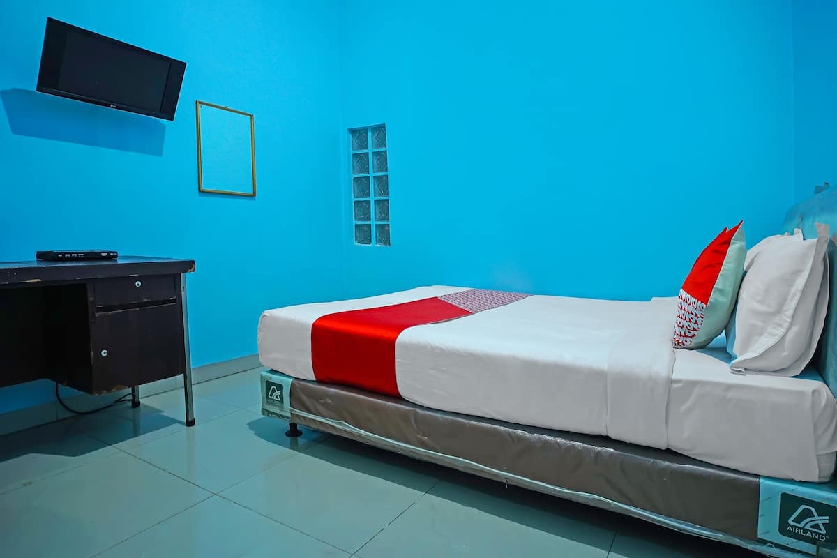 A hotel room with a bed, a TV mounted on the wall, a desk, and a window.