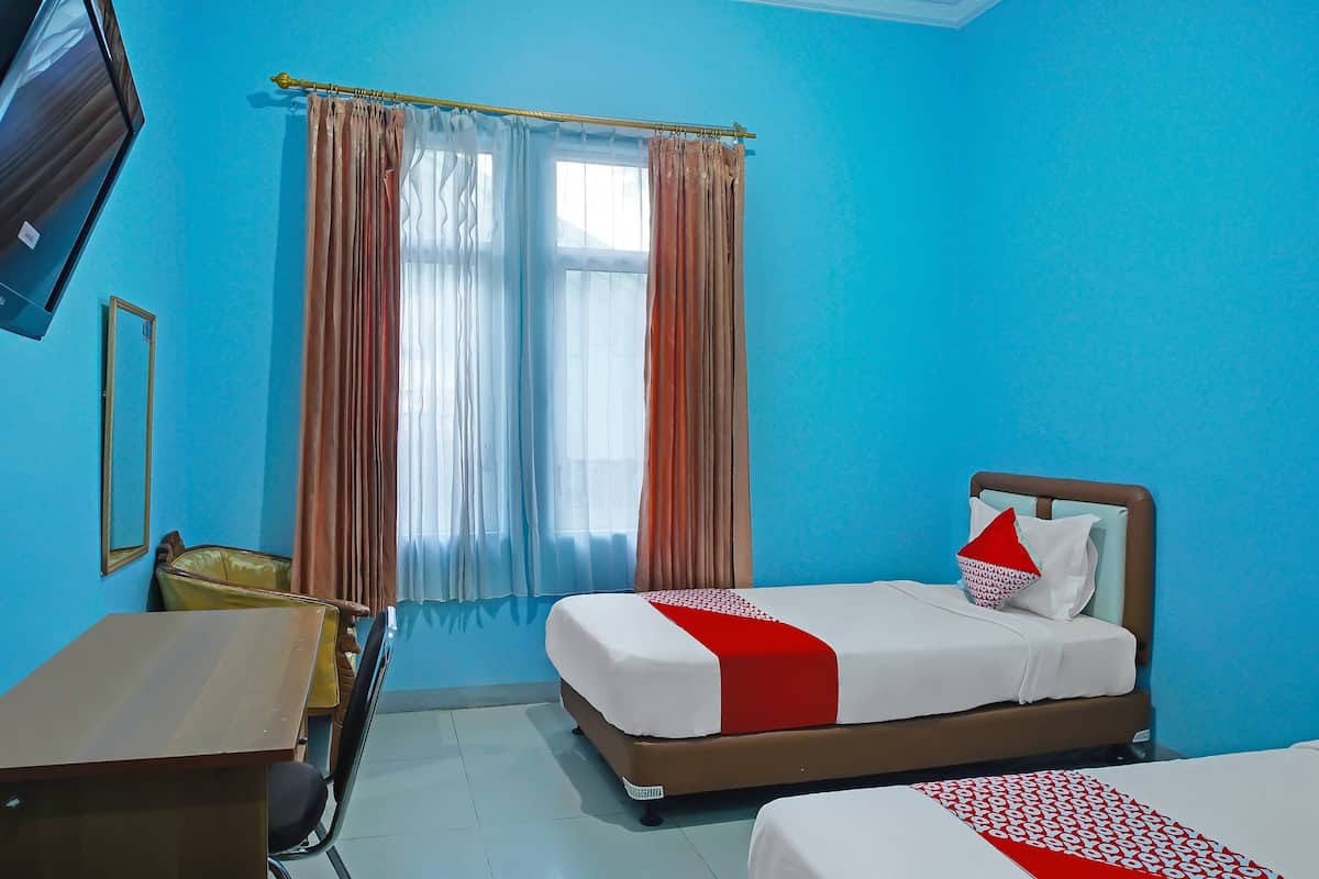 A hotel room with two beds, a desk, a chair, a TV, and a window with curtains.