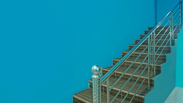 A staircase with metal railings and a ball finial, against a solid blue wall. - Hotel O Sidikalang Near KEJAKSAAN NEGERI DAIRI (Kota Sidikalang)