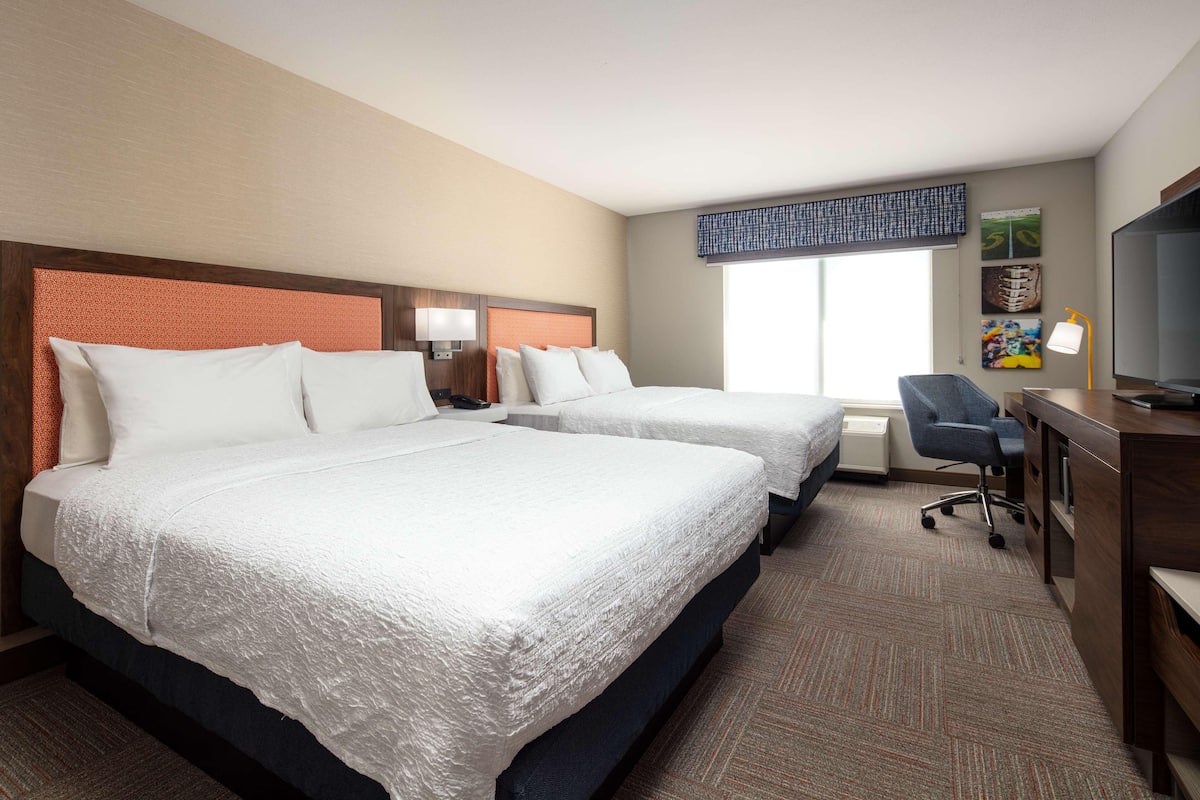 A hotel room with two beds, a desk with a chair, a television, and artwork on the wall.