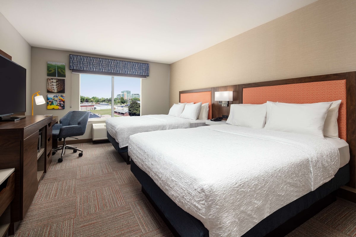 A hotel room with two beds, a desk, a chair, and a TV.