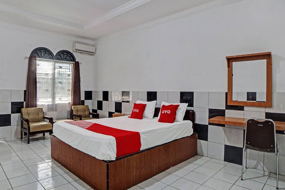 A hotel room with a large bed, two armchairs, a desk, and a mirror.