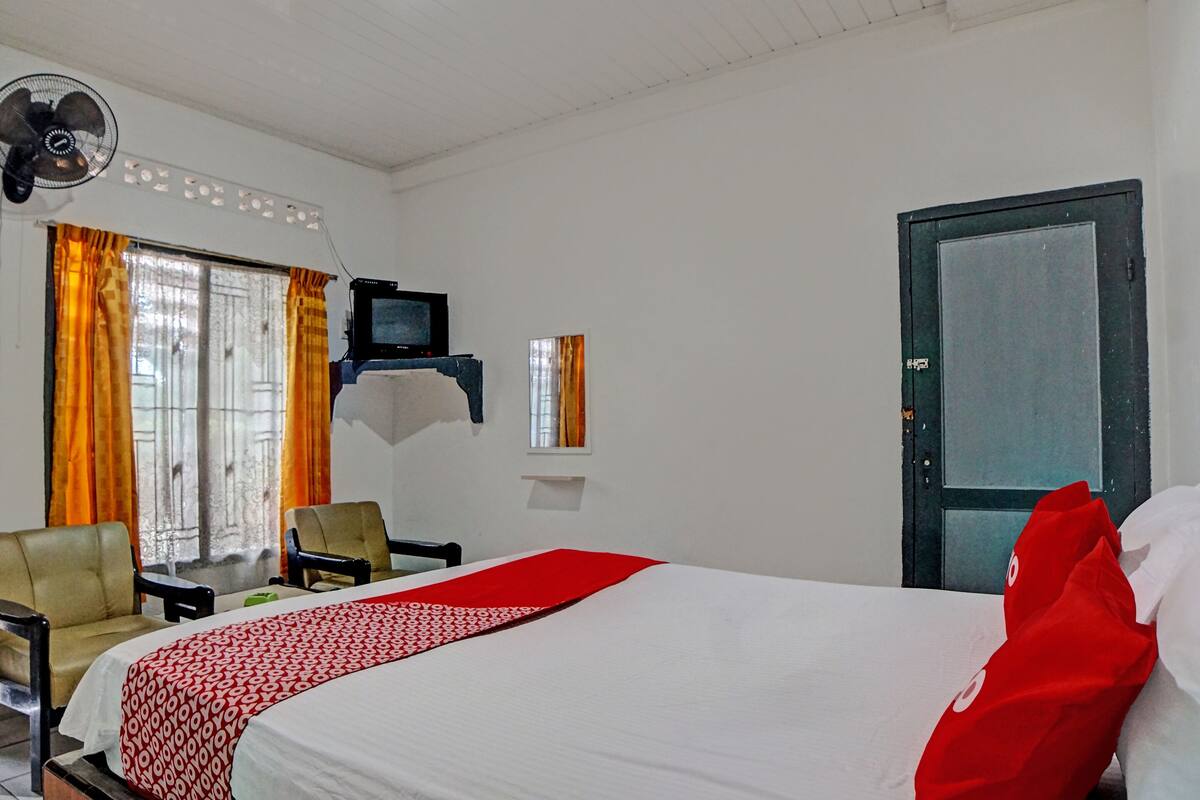 A hotel room with a bed, two chairs, a television, and a window with curtains.