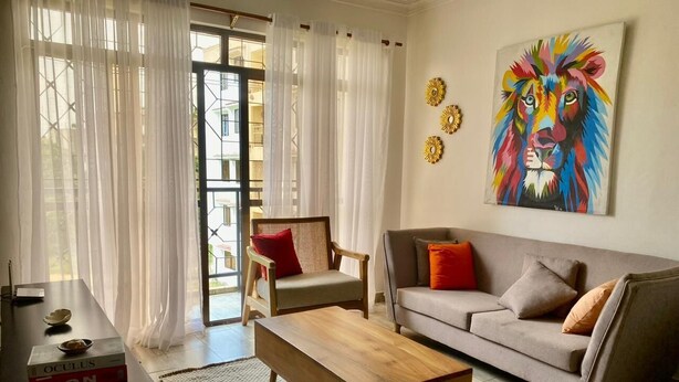 A living room with a sofa, a wooden coffee table, a chair, and a painting on the wall. - Aval Homes-Modern 1 bedroom apartment in Bamburi (Mombasa)